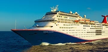 A large modern cruise ship, the Carnival Elation, photographed in open ocean under clear blue