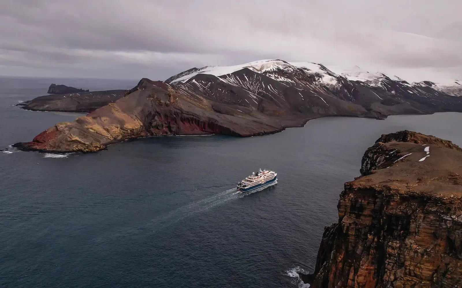 A small expedition cruise ship navigates turquoise waters surrounded by dramatic volcanic islands