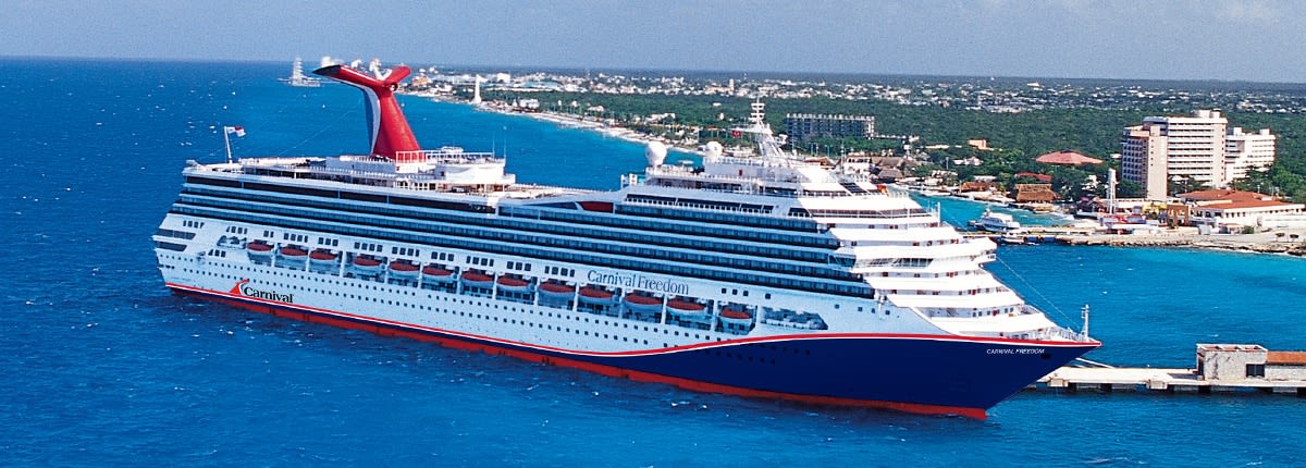 A large Carnival cruise ship docked at a coastal destination, featuring a distinctive red, white