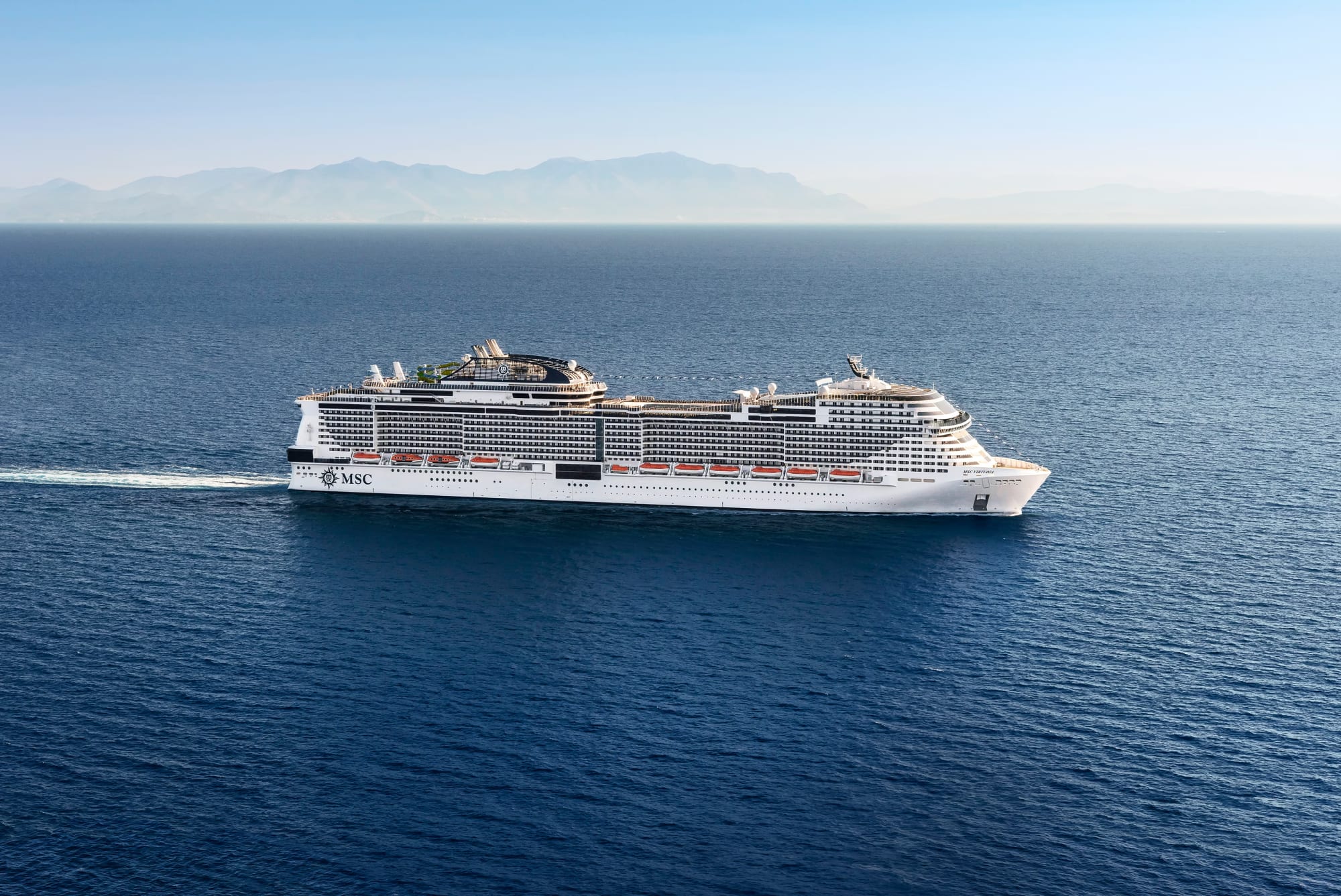 A modern large cruise ship operated by MSC Cruises sails through calm Mediterranean waters