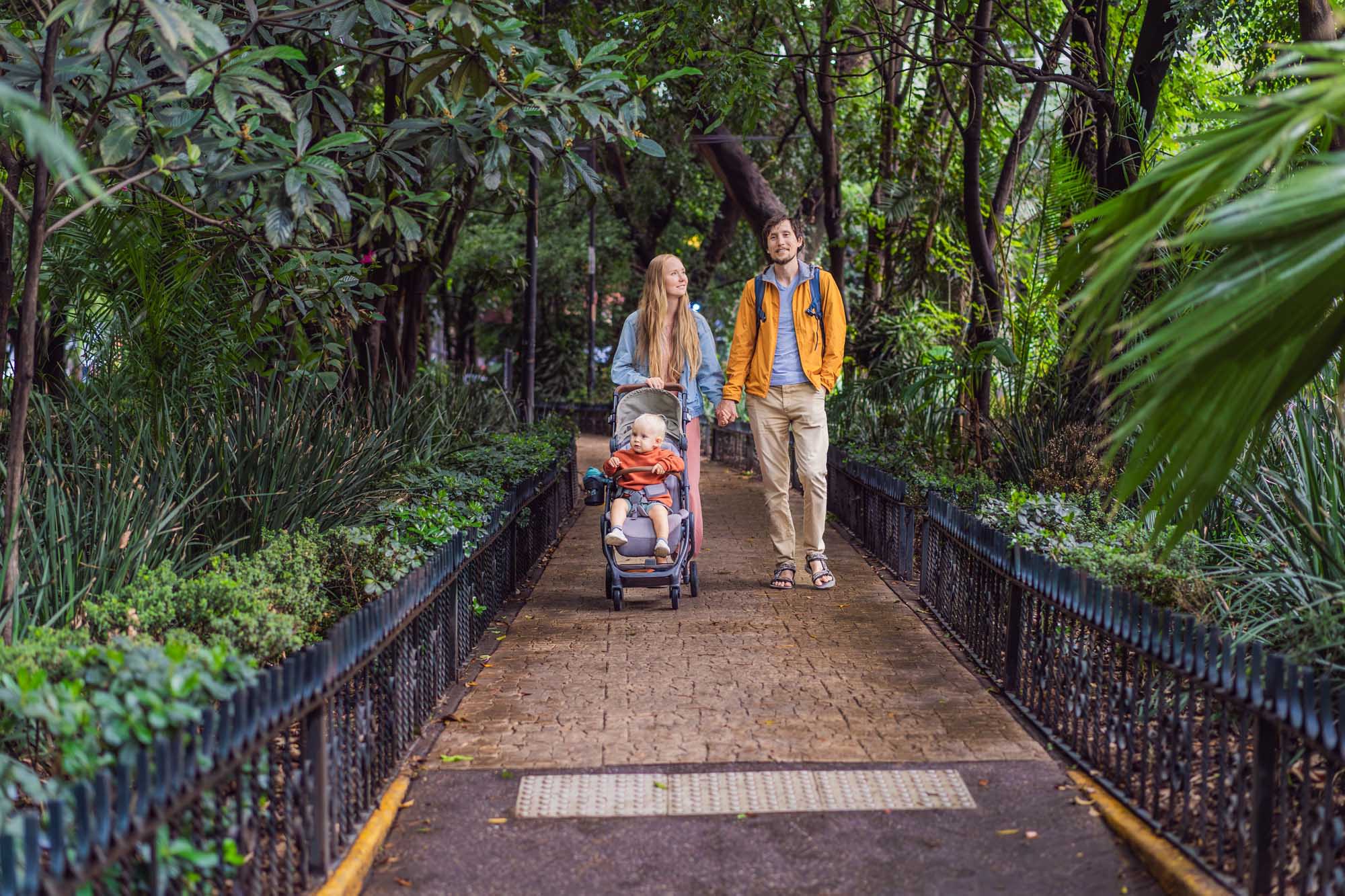 A young family with a toddler in a stroller walks along a tree-lined pedestrian pathway in