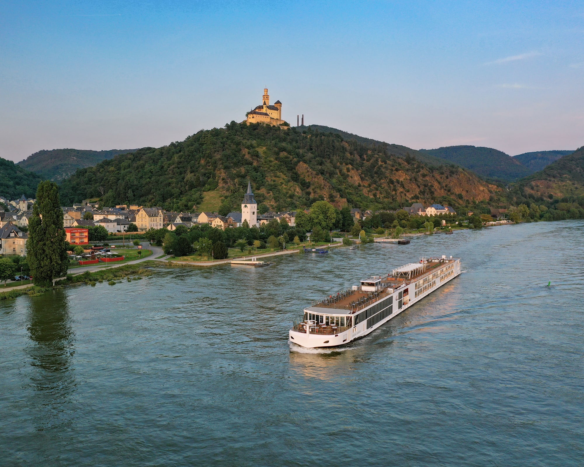 A scenic river cruise ship navigates past the charming town of Braubach on the Rhine River