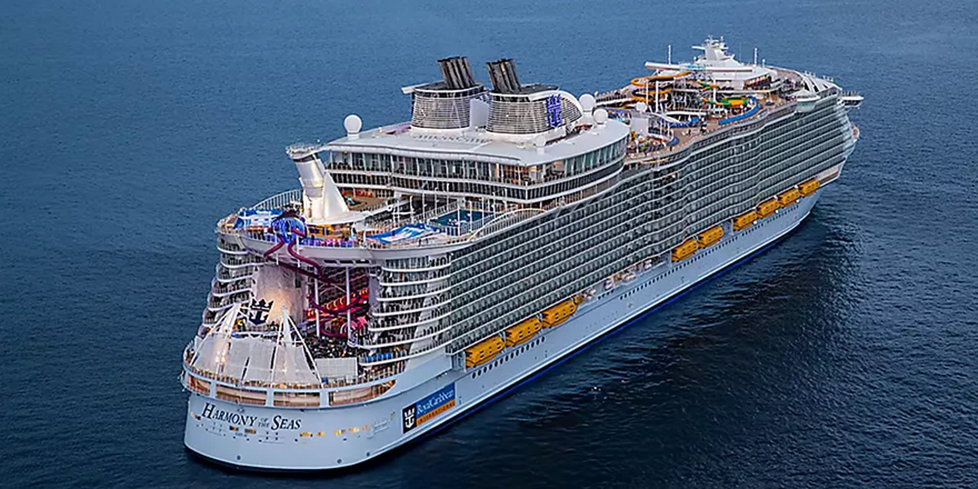 An aerial photograph of a massive modern cruise ship at sea, showcasing its distinctive white hull