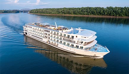 A large, multi-deck river cruise ship navigates the calm waters of the Mississippi River