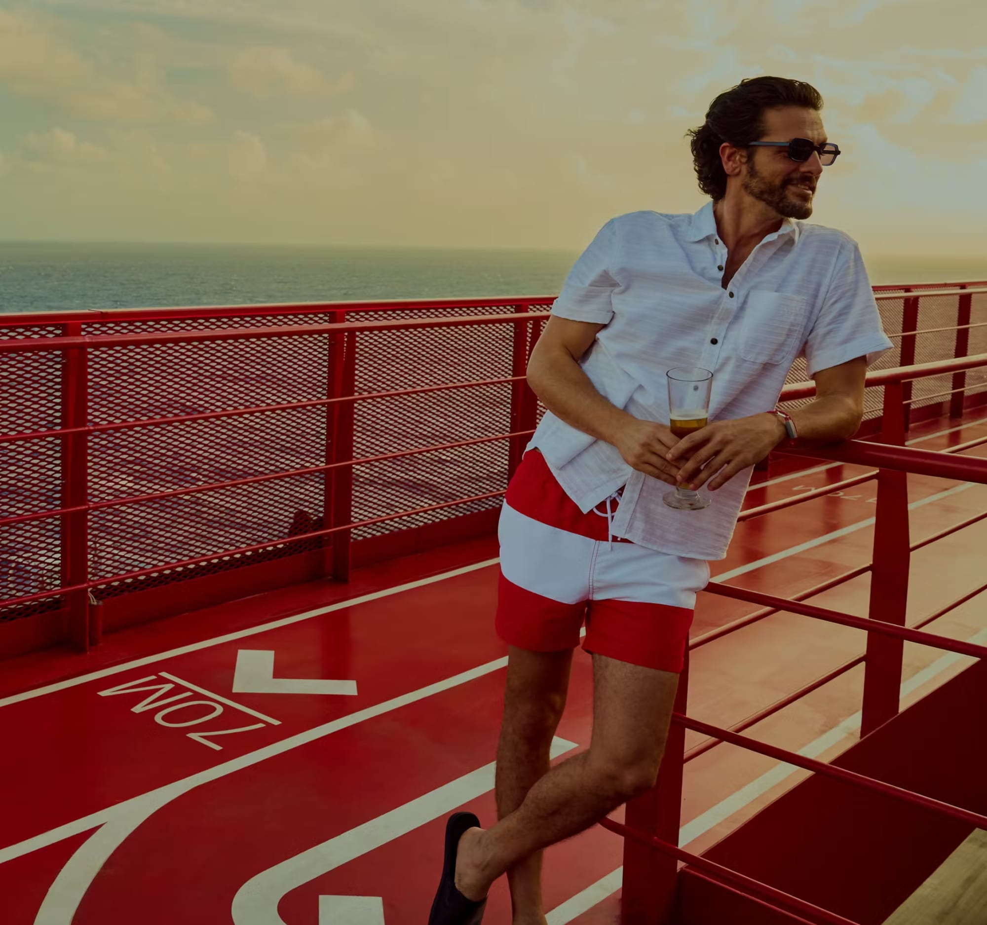 A man in a light blue short-sleeved shirt and red shorts stands on the red and white deck of