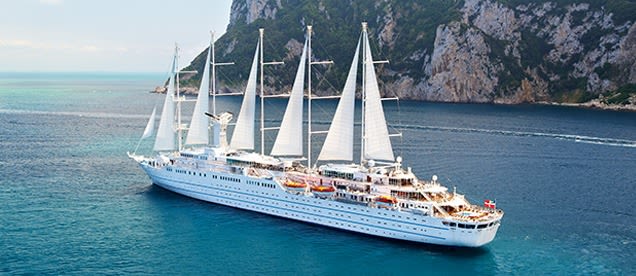A luxurious white sailing yacht with multiple masts anchored in turquoise Mediterranean waters near
