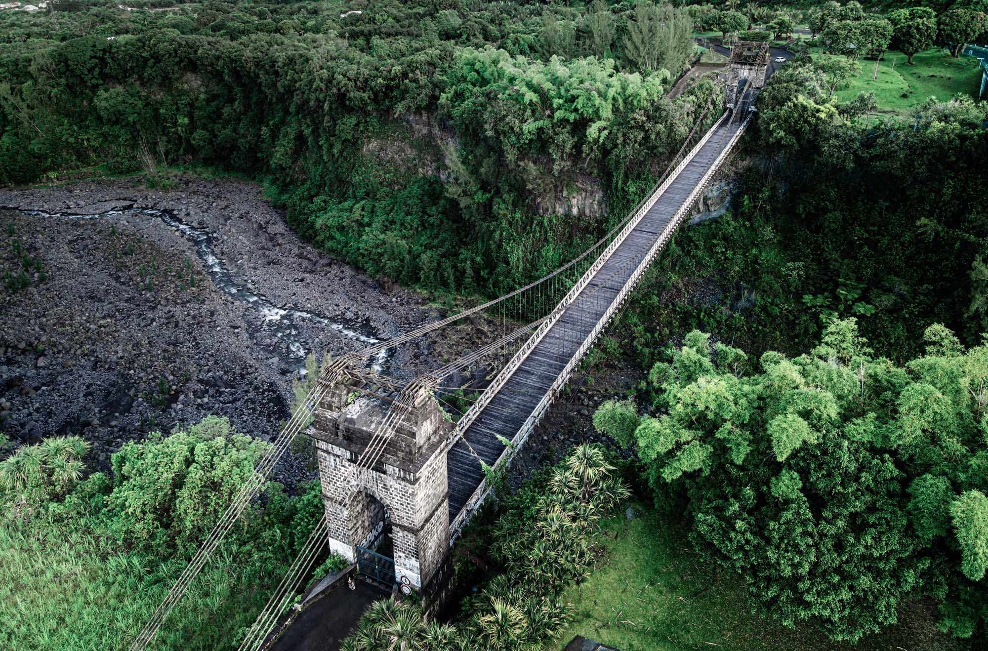 An aerial view of a long wooden suspension bridge spanning across a lush, dense tropical forest