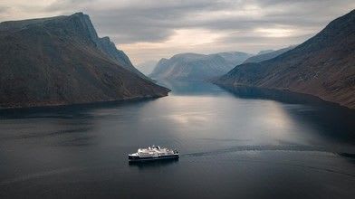 A passenger cruise ship navigates through a dramatic Norwegian fjord surrounded by steep mountain