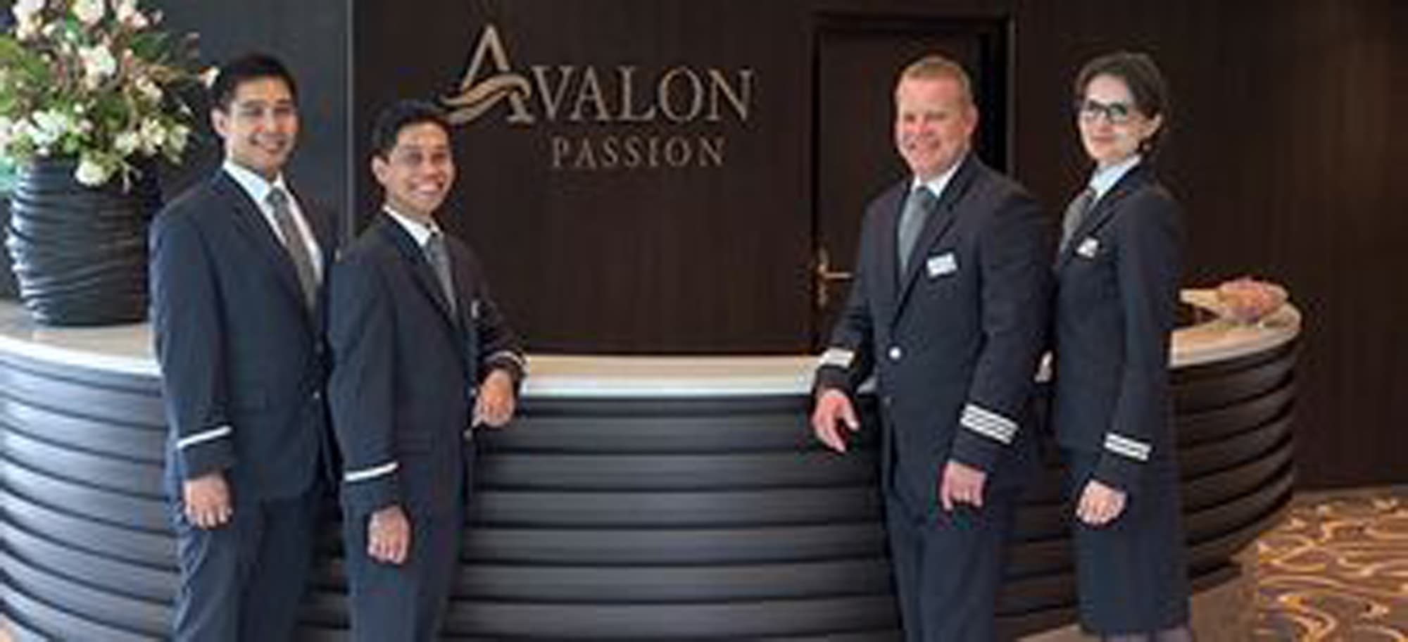 Five uniformed staff members stand formally at the entrance to the Avalon Passion, a river cruise
