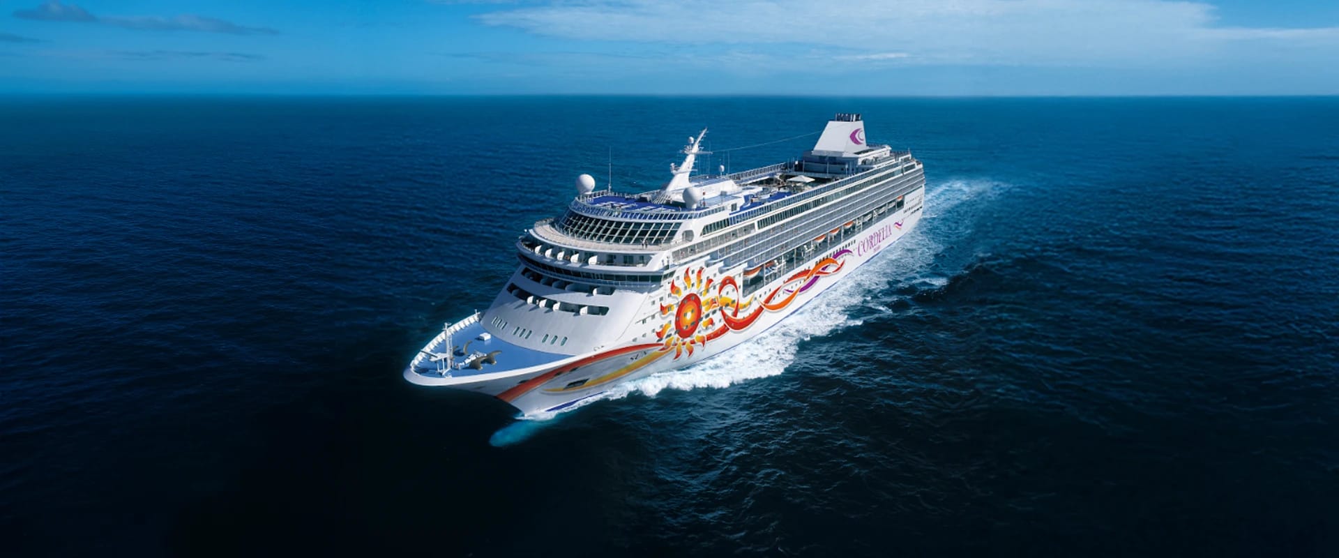 A colorful cruise ship with a vibrant sun-like graphic design sailing across deep blue waters under