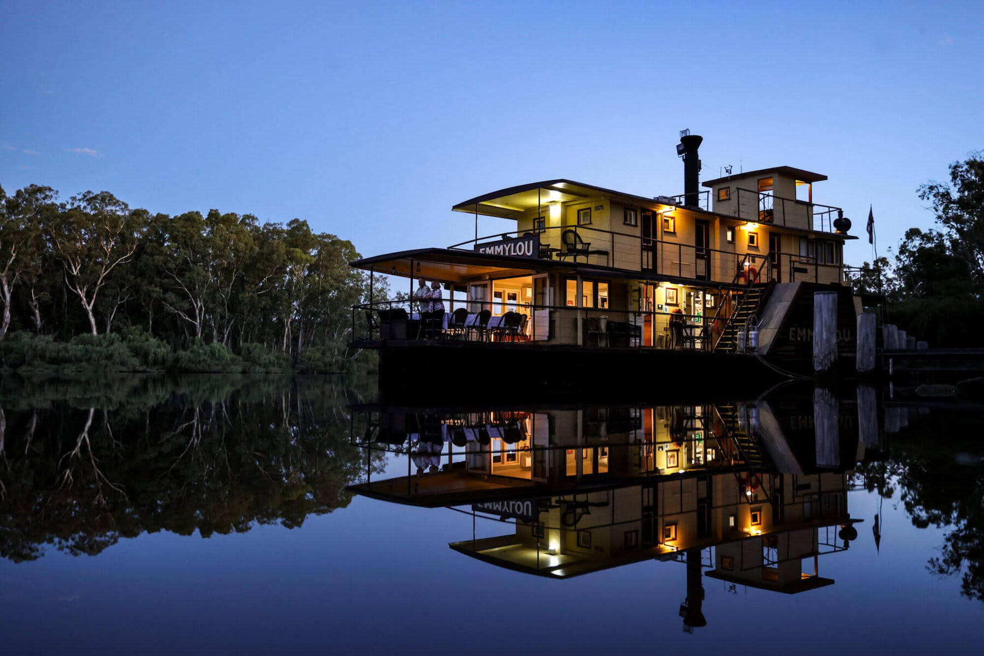 A beautifully illuminated luxury riverboat named Emmylou is perfectly mirrored in the calm waters