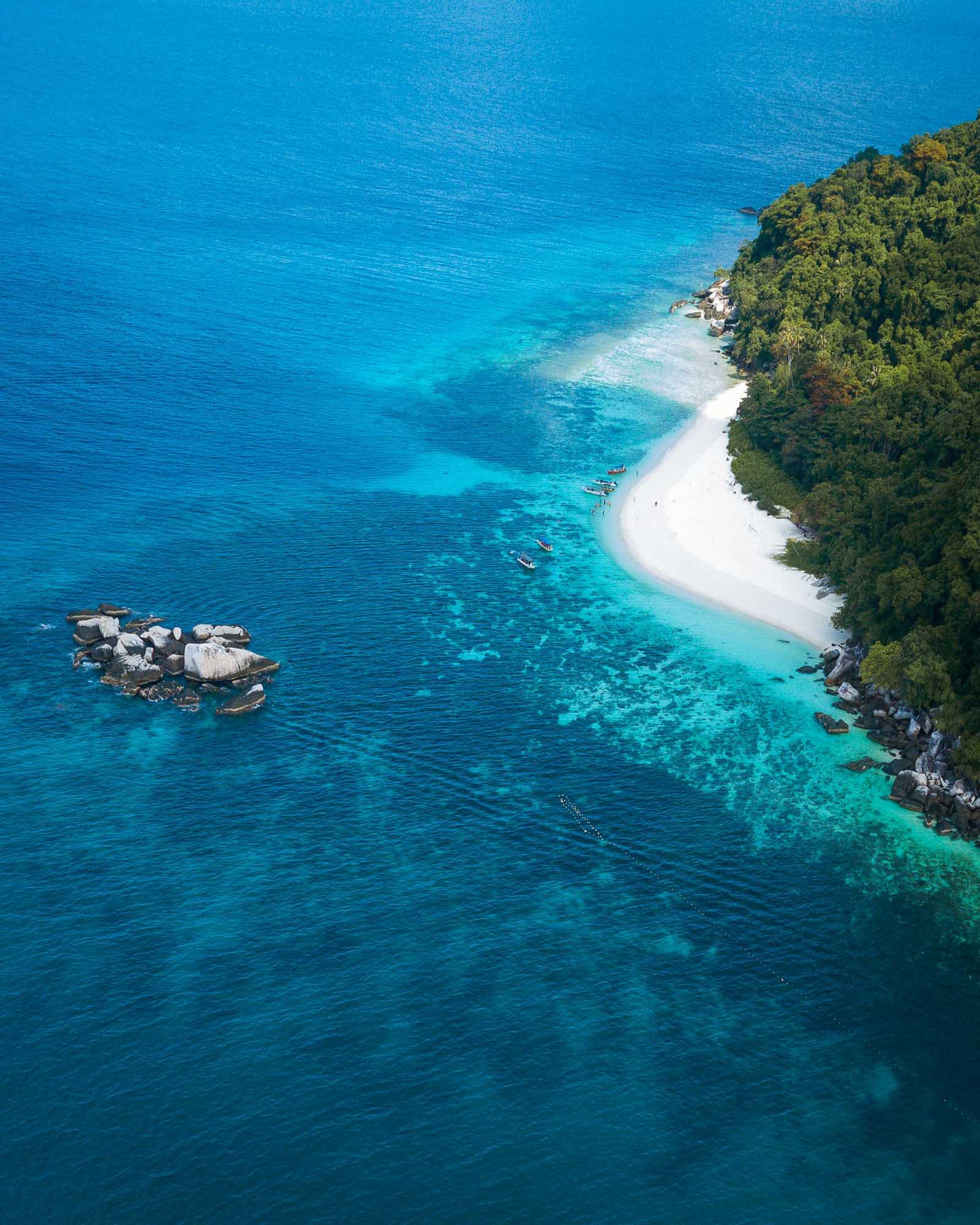 An aerial view of a secluded white sand beach bordered by lush tropical forest on the right