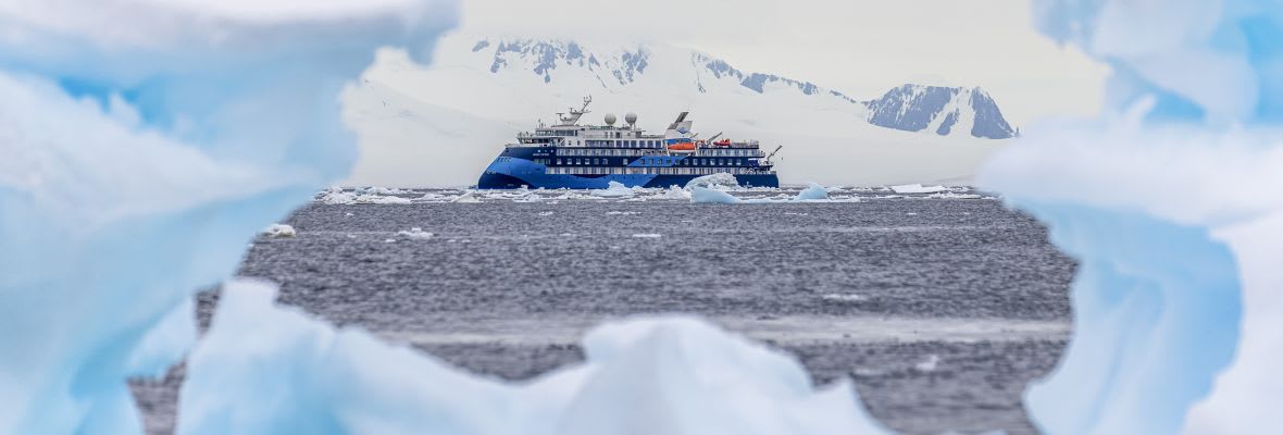 A modern expedition cruise ship navigates through icy Antarctic waters, framed by massive icebergs