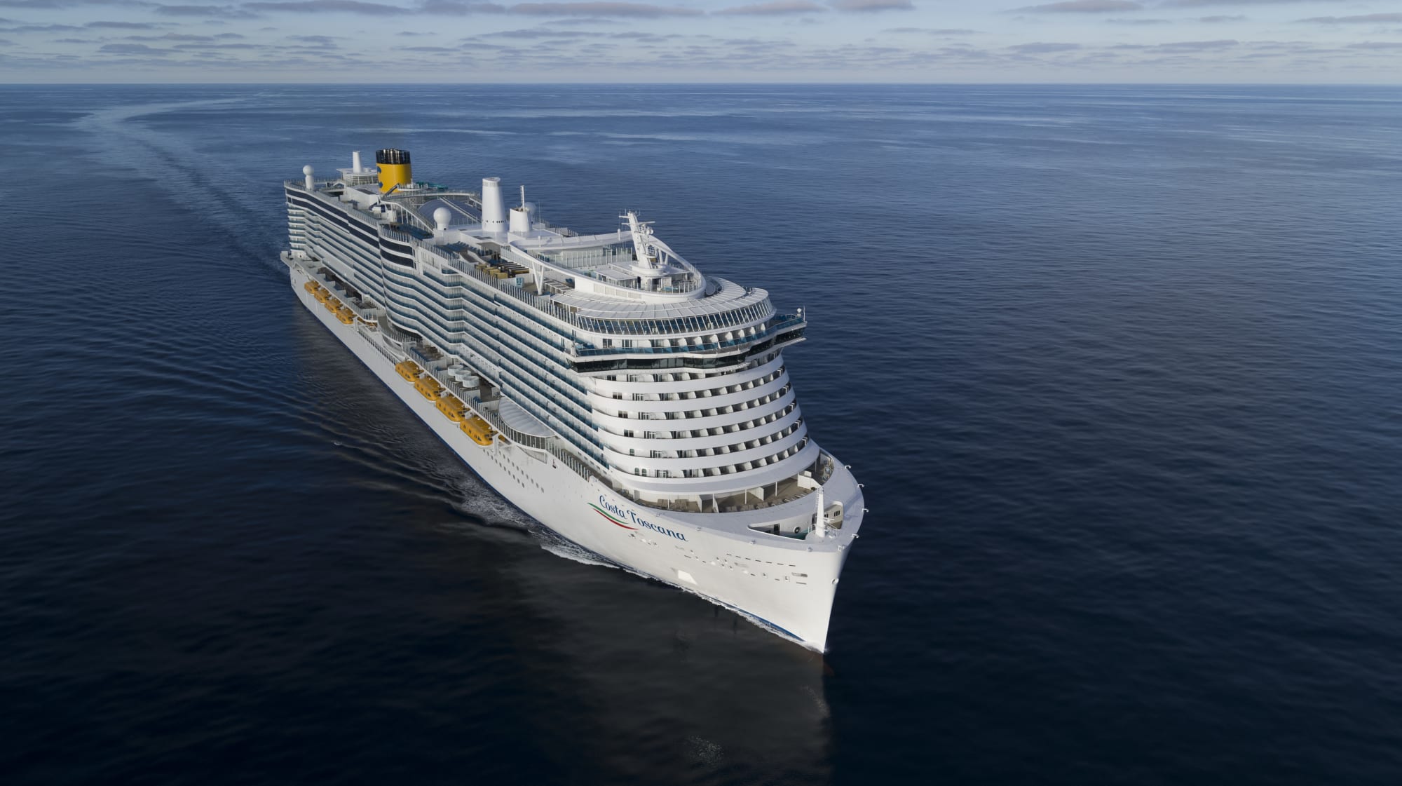 A large white cruise ship with yellow and white color scheme sailing across a serene, flat blue ocean under an overcast sky. The vessel appears to be a modern, sleek cruise liner with multiple decks and balconies.