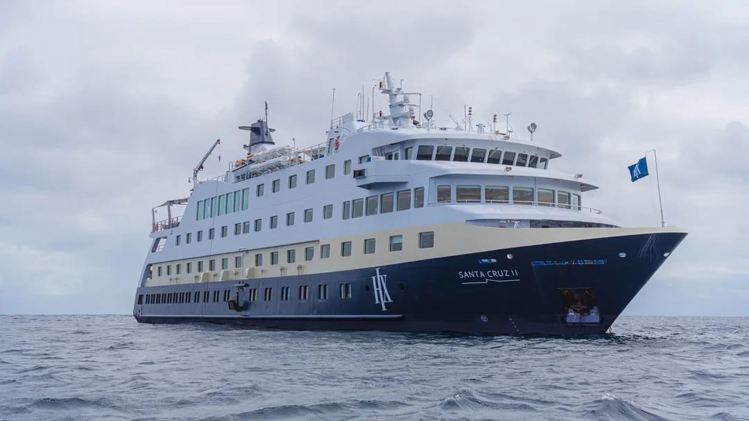 A sleek white and navy blue expedition cruise ship sailing on a gray, overcast ocean. The vessel appears to be a small to mid-sized expedition-style ship designed for adventure travel.