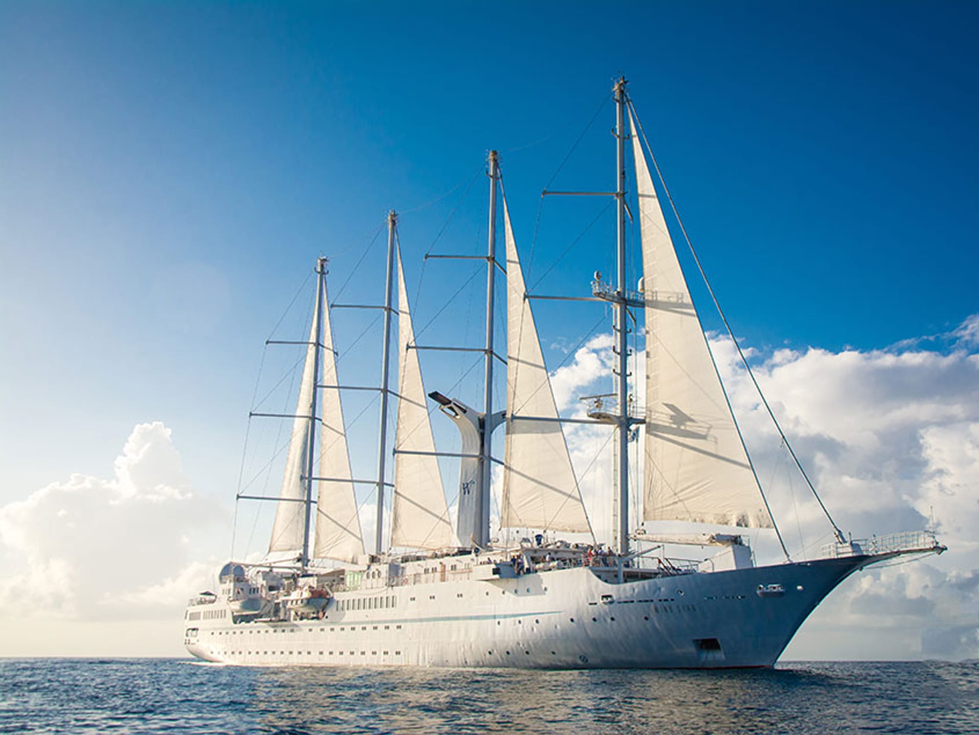 A pristine white multi-masted sailing vessel with fully unfurled white sails cruising on blue ocean