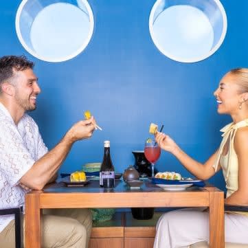 A man and woman enjoy a romantic dinner date at a restaurant with a vibrant blue wall and circular