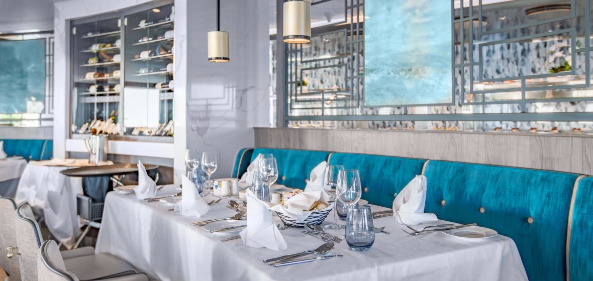 Elegant fine dining restaurant aboard an expedition cruise ship with ocean views through large windows.