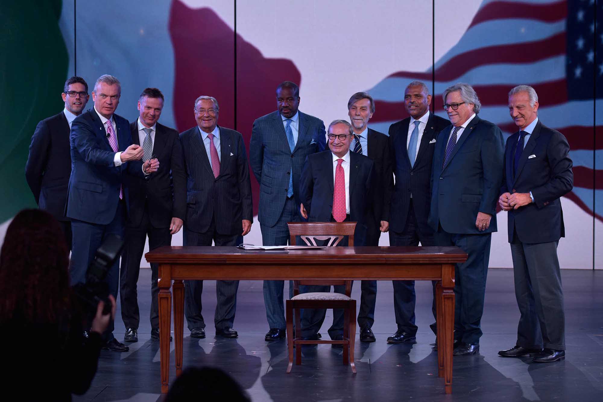 A formal gathering of nine well-dressed men in business suits positioned around a wooden desk on