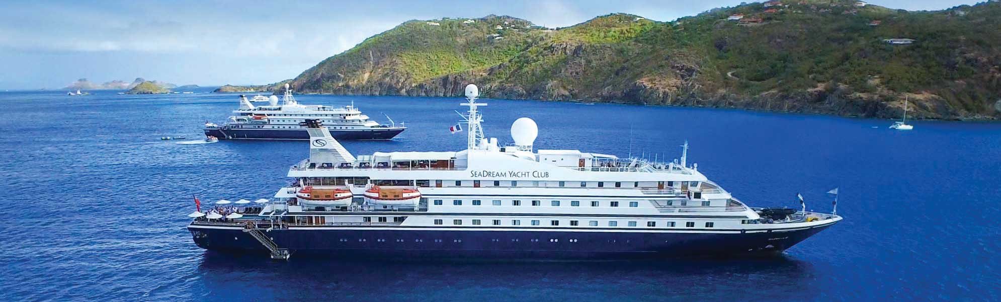 The luxury expedition yacht SeaDream Yacht Club is anchored in crystalline blue waters near a lush