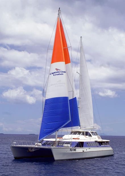 A striking catamaran sailboat with tri-color sails (orange, white, and blue) matching the Captain