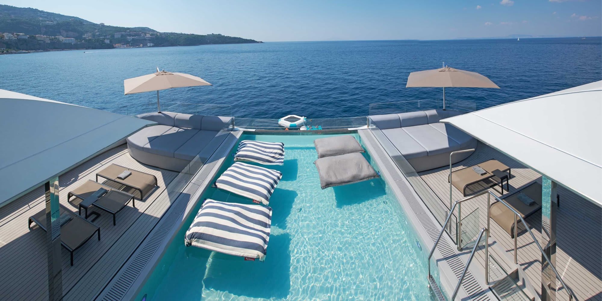 A stunning aerial view of a modern cruise ship's pool deck featuring a turquoise infinity pool