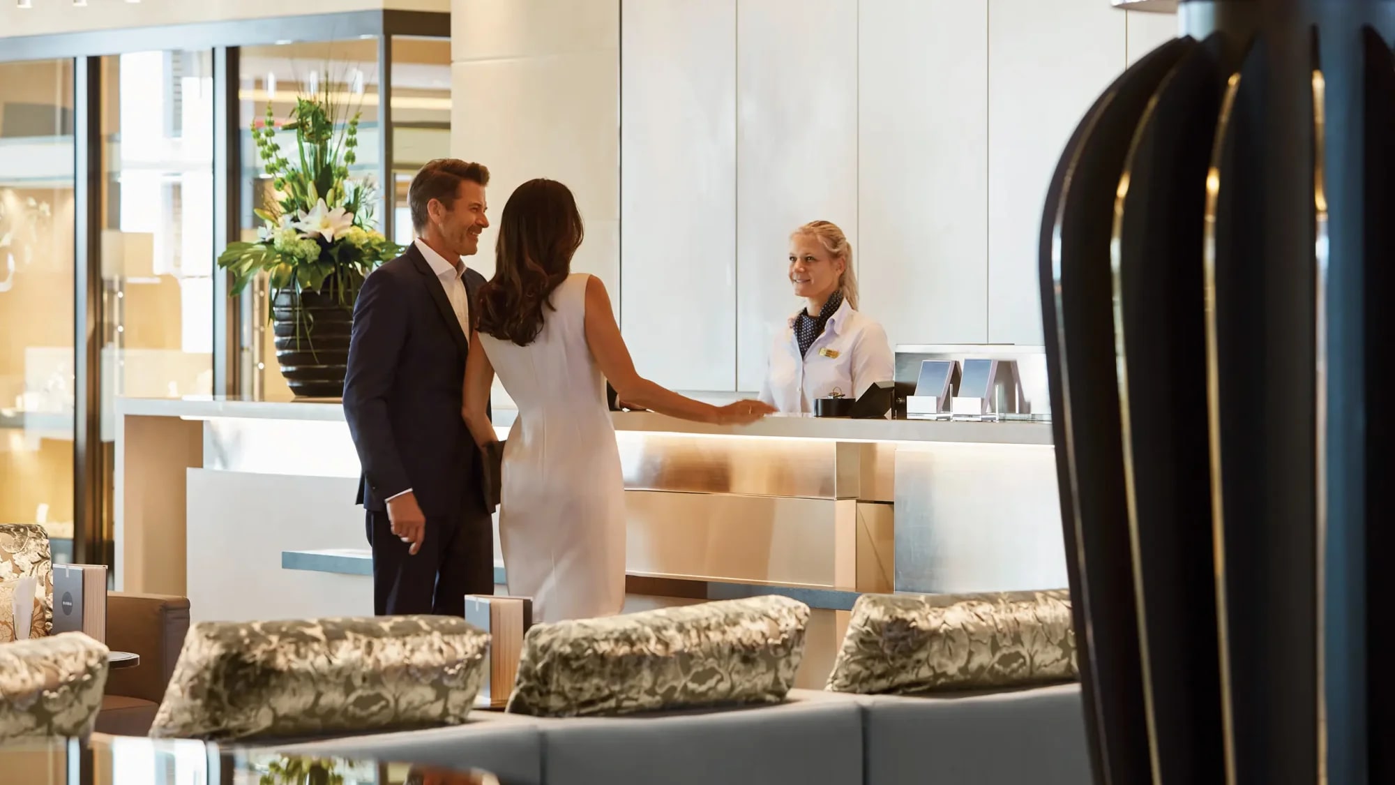 A sophisticated hotel lobby scene showing a well-dressed couple checking in at a modern reception