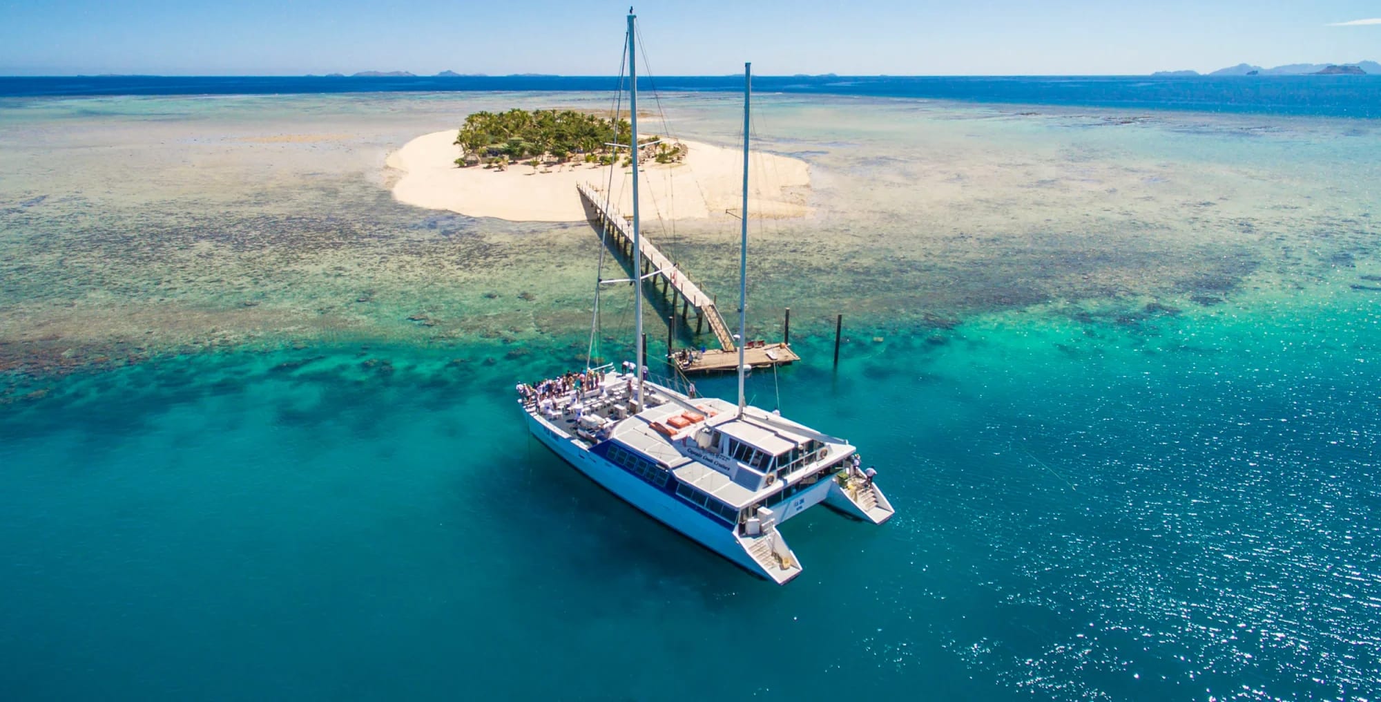 A blue and white catamaran anchors in crystal-clear turquoise waters near a pristine white sand