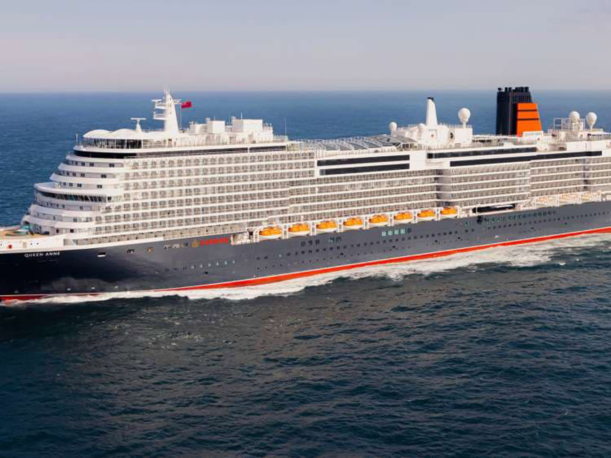 A large modern cruise ship identified as Queen Anne sailing on open ocean waters. The vessel