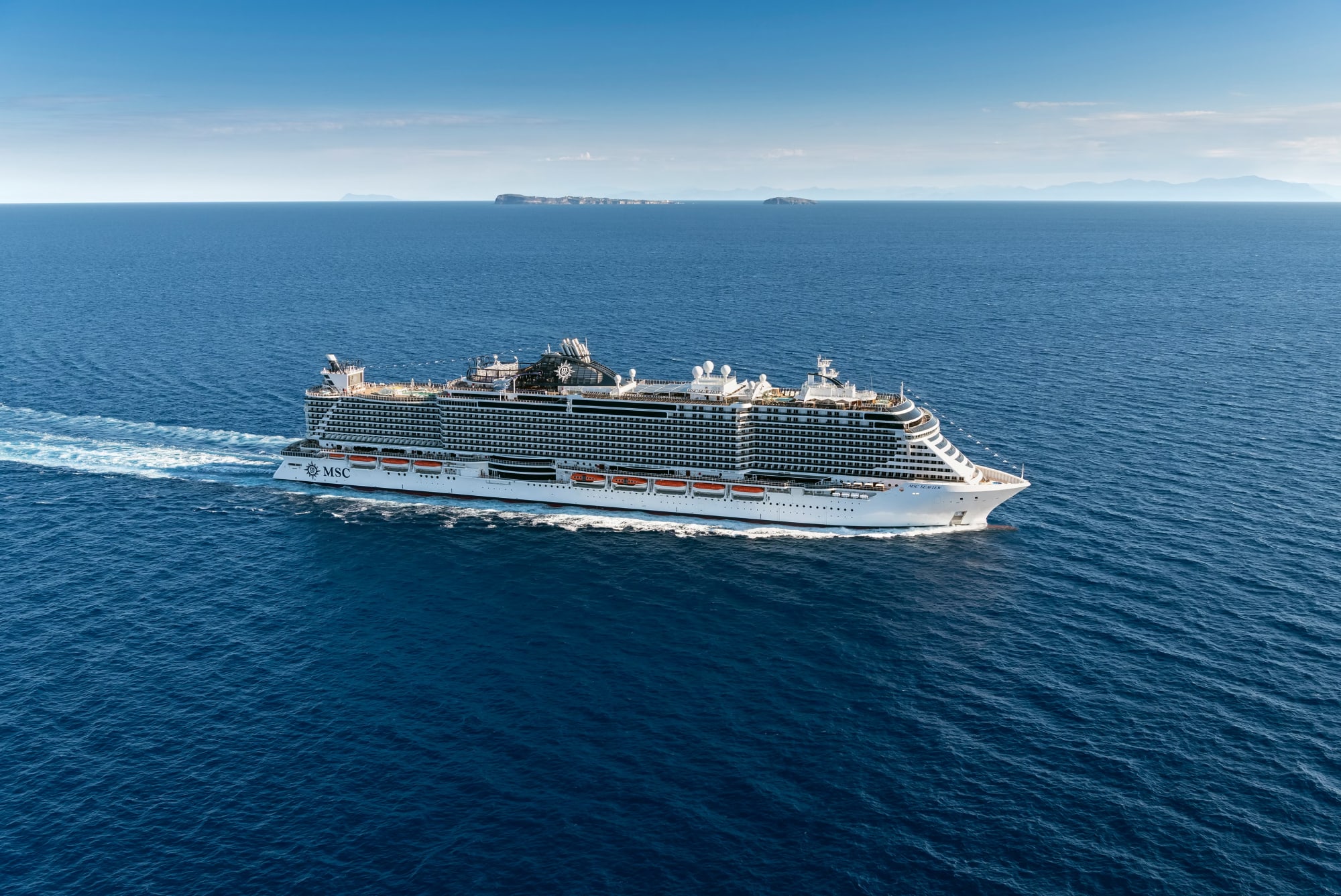 A large modern cruise ship operated by MSC Cruises sails through open ocean waters under clear blue