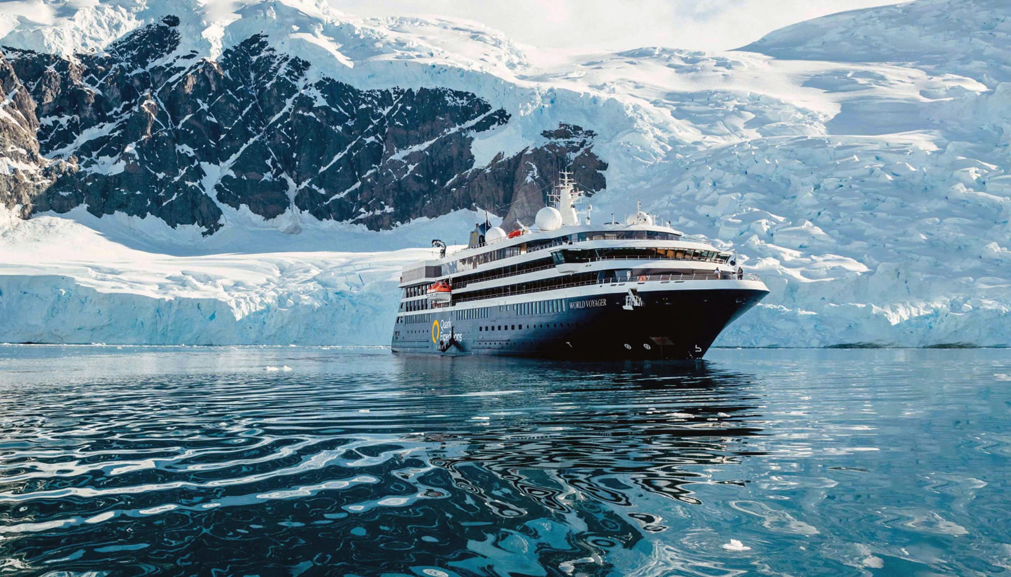 A modern expedition cruise ship navigating through icy blue waters surrounded by snow-covered rocky