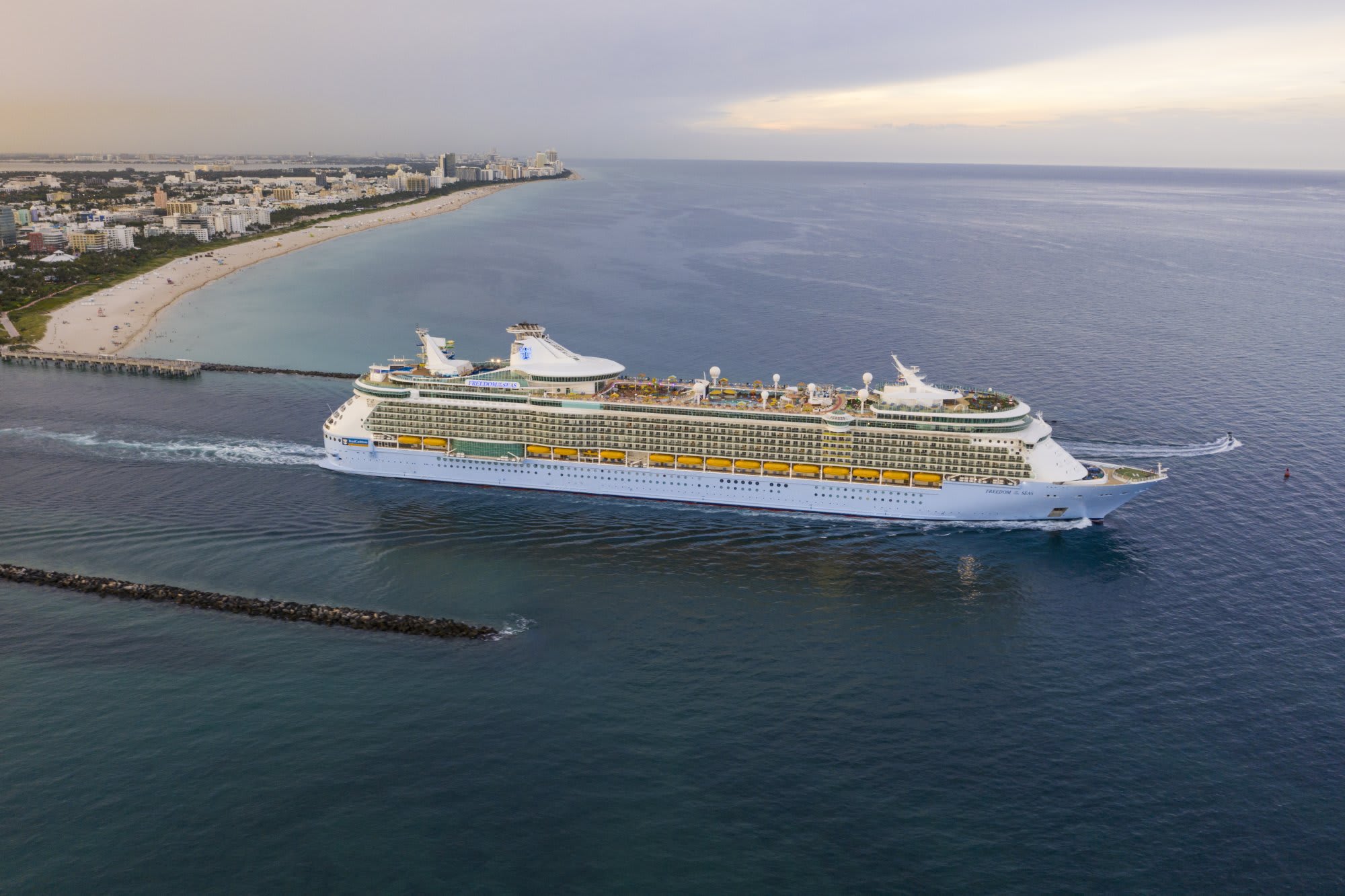 A massive Royal Caribbean cruise ship departs from the Port of Miami, with the city's beachfront