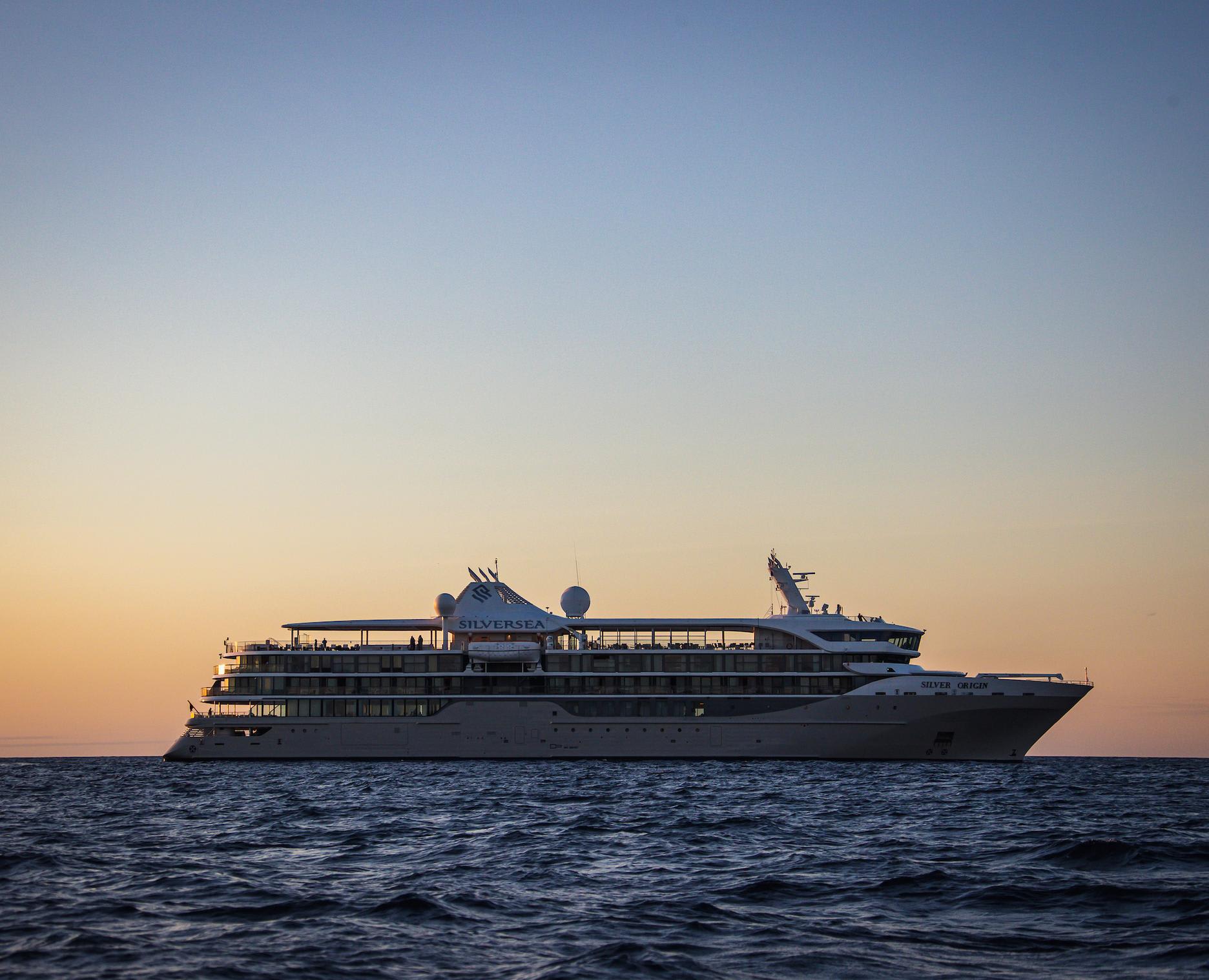 A luxury expedition cruise ship, the Silver Discoverer, is anchored in calm waters at golden hour