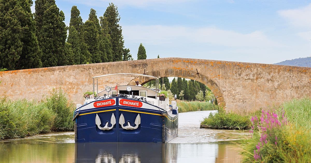 The MS Enchante, a luxury river cruise barge, navigates through a picturesque European canal