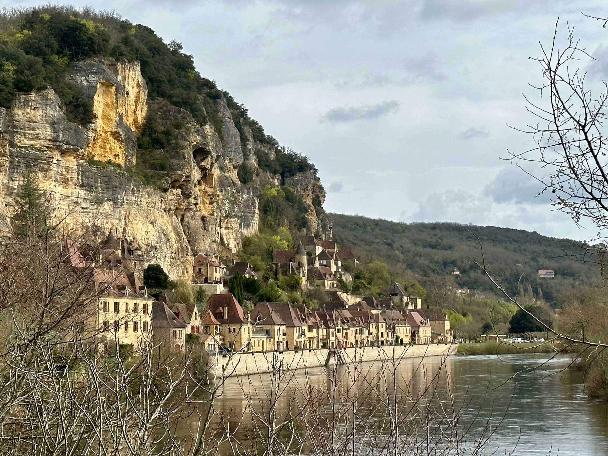 A picturesque medieval village nestled along a river beneath dramatic limestone cliffs, featuring
