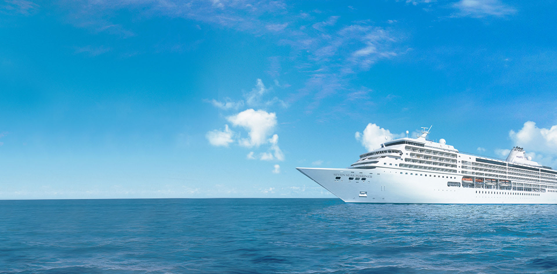 A large, white luxury cruise ship sailing on a calm, azure blue ocean under a bright, cloud-dotted sky. The vessel appears sleek and modern, cutting through pristine maritime waters.