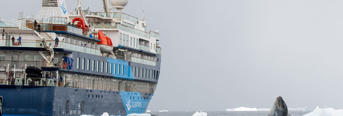 Expedition cruise ship navigating through Arctic sea ice with dramatic polar landscape.
