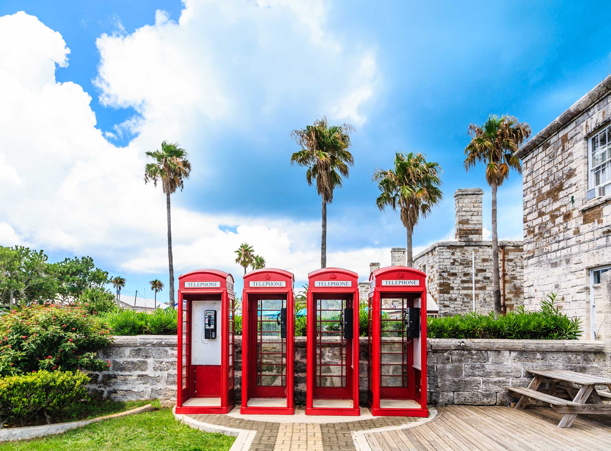 Four iconic red British telephone booths stand in a row against a backdrop of colonial stone