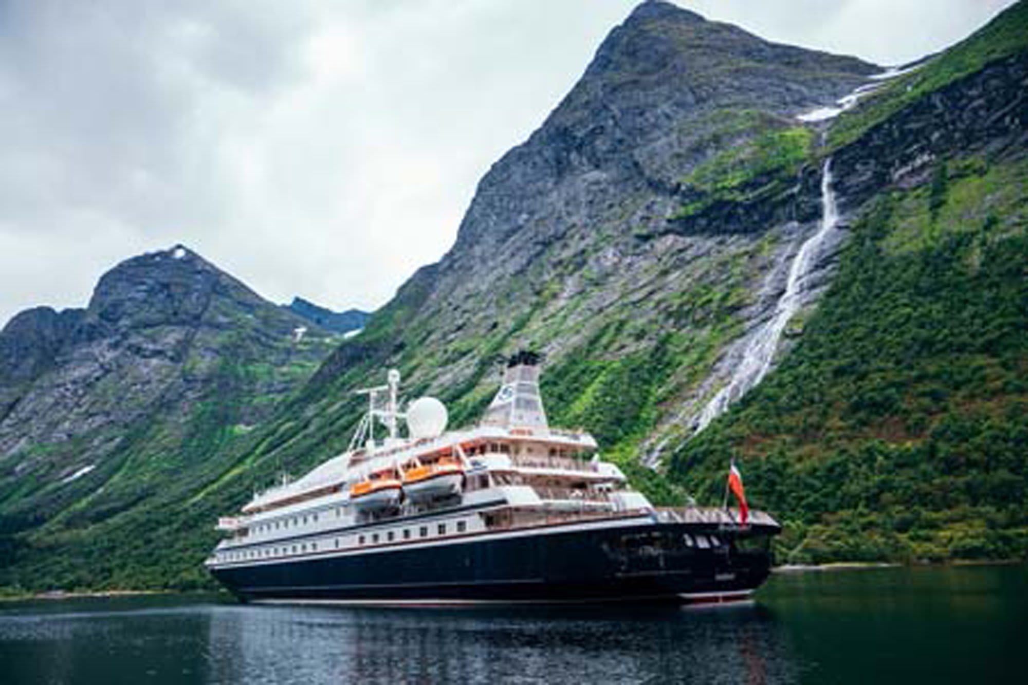 A large expedition cruise ship anchors in a dramatic Norwegian fjord, surrounded by steep