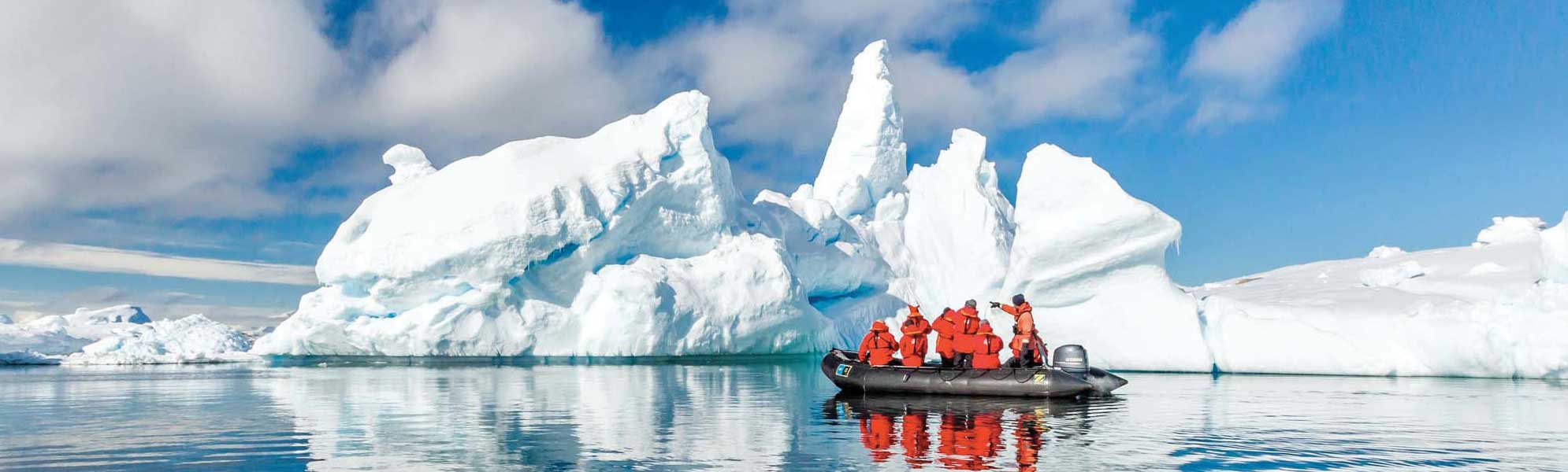 A small black expedition Zodiac boat with passengers in bright orange safety gear navigates calm