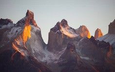 Towering granite peaks bathed in warm golden and orange light during sunset or sunrise, with snow