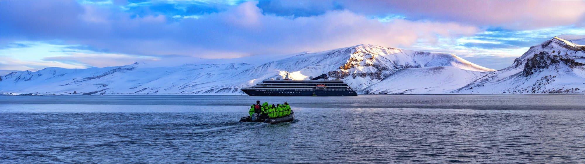 A luxury expedition cruise ship anchored in a pristine Arctic bay with snow-capped mountains in