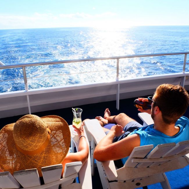 A passenger enjoys a leisurely afternoon on a cruise ship's deck, relaxing in a lounge chair with