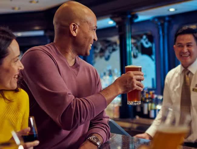 A group of well-dressed passengers enjoy cocktails and conversation at an elegant onboard bar