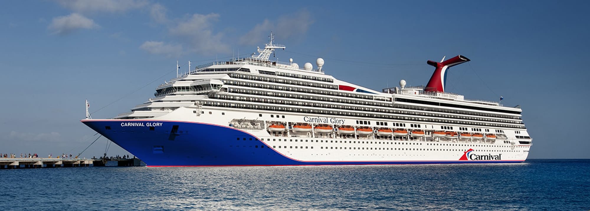 A large Carnival cruise ship docked at a pier, showcasing its blue hull, white superstructure