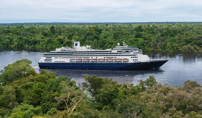 A dark blue and white cruise ship navigating through a narrow river surrounded by dense, green