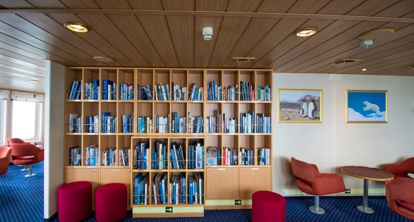 A contemporary library lounge aboard a cruise ship, featuring extensive wooden shelving filled