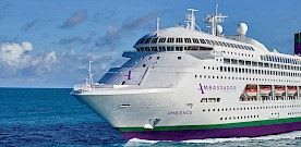 A large modern cruise ship with distinctive purple hull and white superstructure is docked at