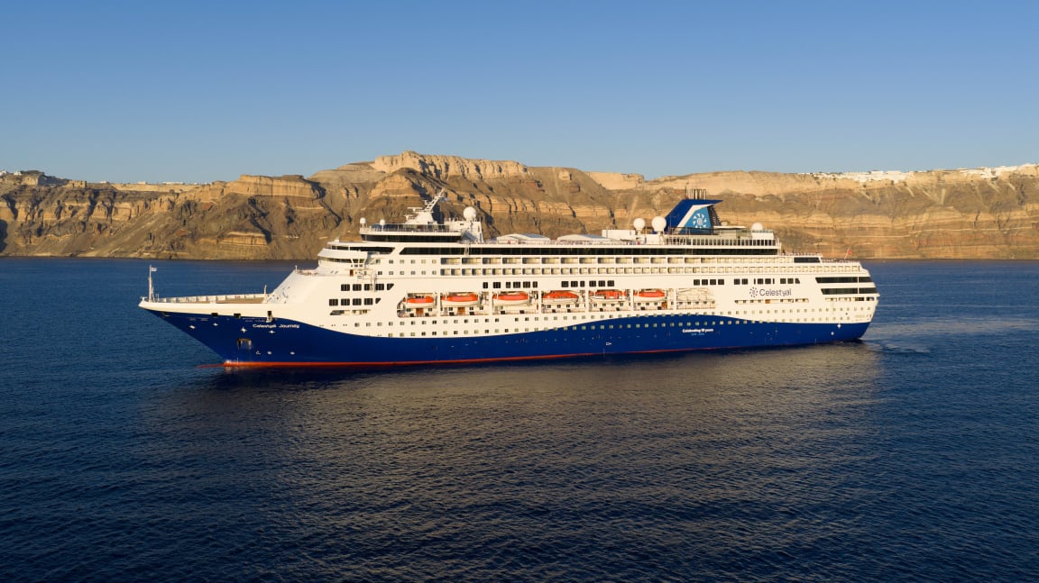 A modern cruise ship operated by Celestyal Cruises is anchored in the azure waters off Santorini