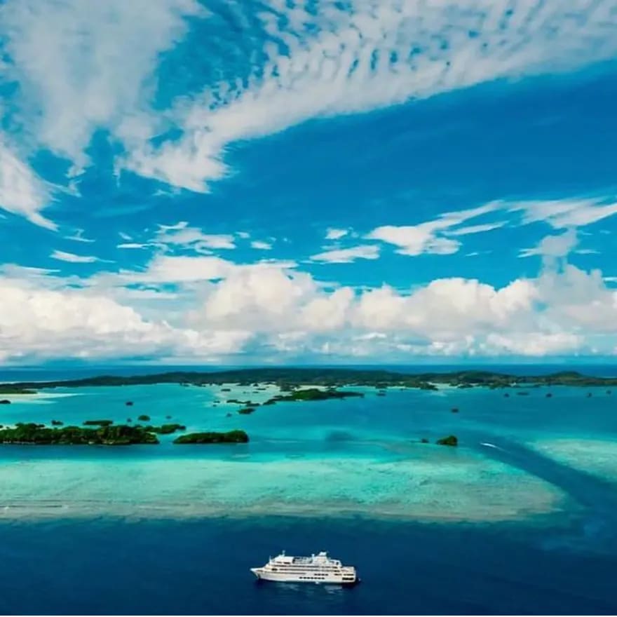 An aerial view of a modern cruise ship anchored in crystal-clear turquoise waters surrounded